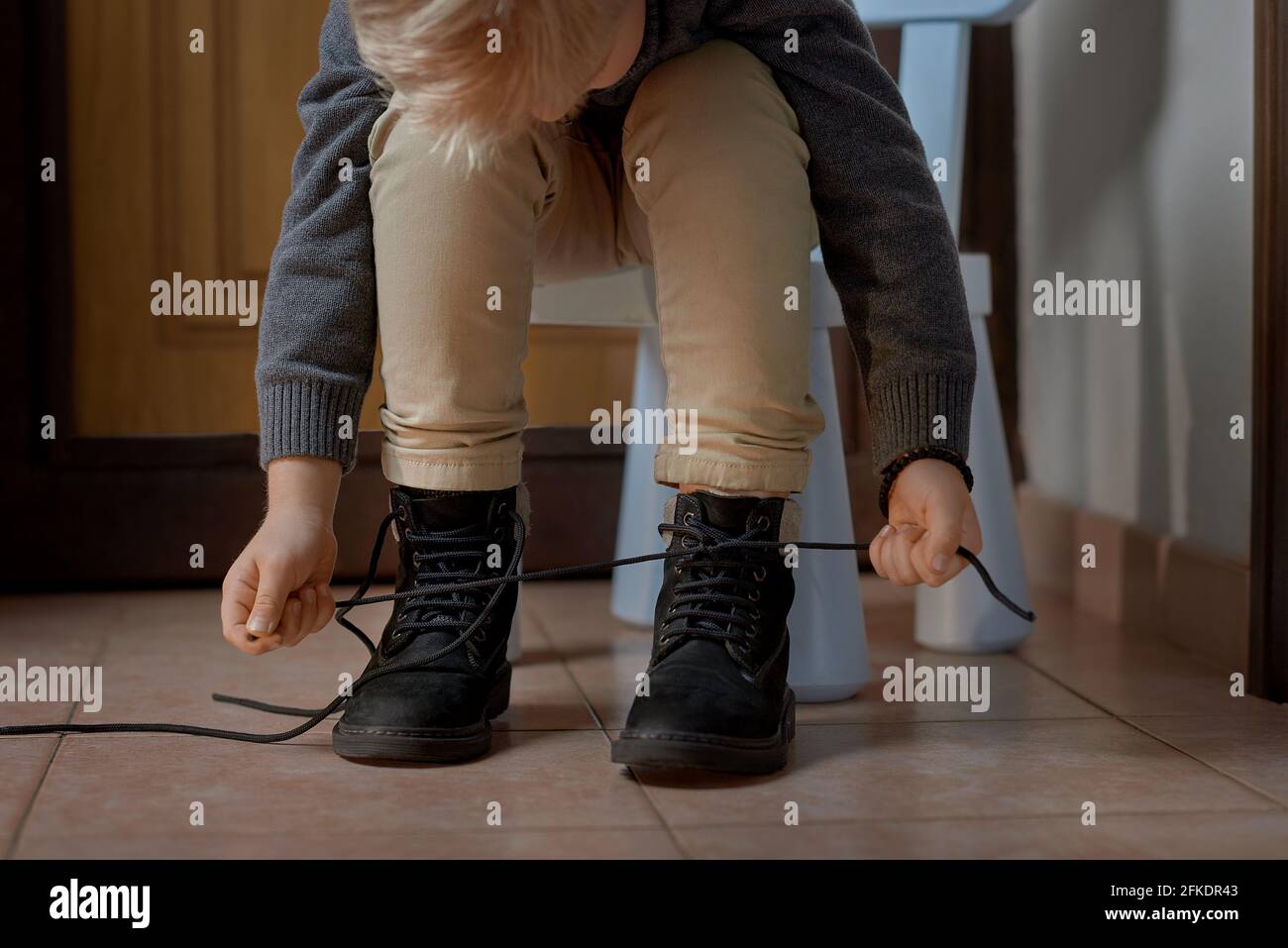 Child tying the laces on boots before leaving home, selective focus Stock Photo