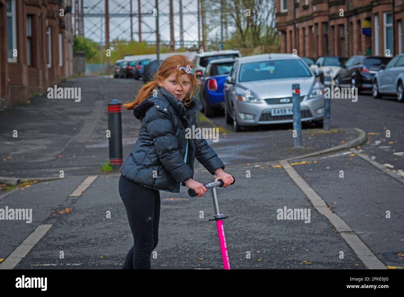A girl with ginger hair riding a scooter with Temple Gasworks in backround  , Glasgow , Scotland Stock Photo