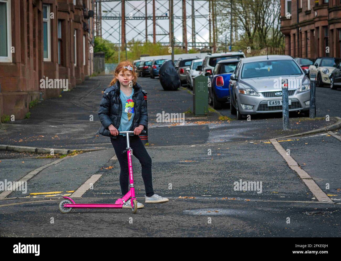 A girl with ginger hair riding a scooter with Temple Gasworks in backround  , Glasgow , Scotland Stock Photo