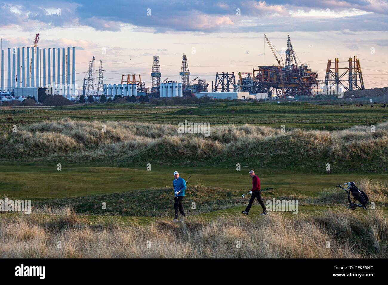 Golf player playing at Seaton Carew Golf Club with the Top Deck of Shell Brent offshore platform being dismantled and recycled at Able UK in distance Stock Photo