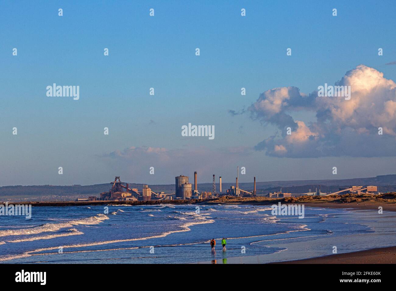 Couple walking along the beach with the Redcar steelworks in distance , England, UK Stock Photo