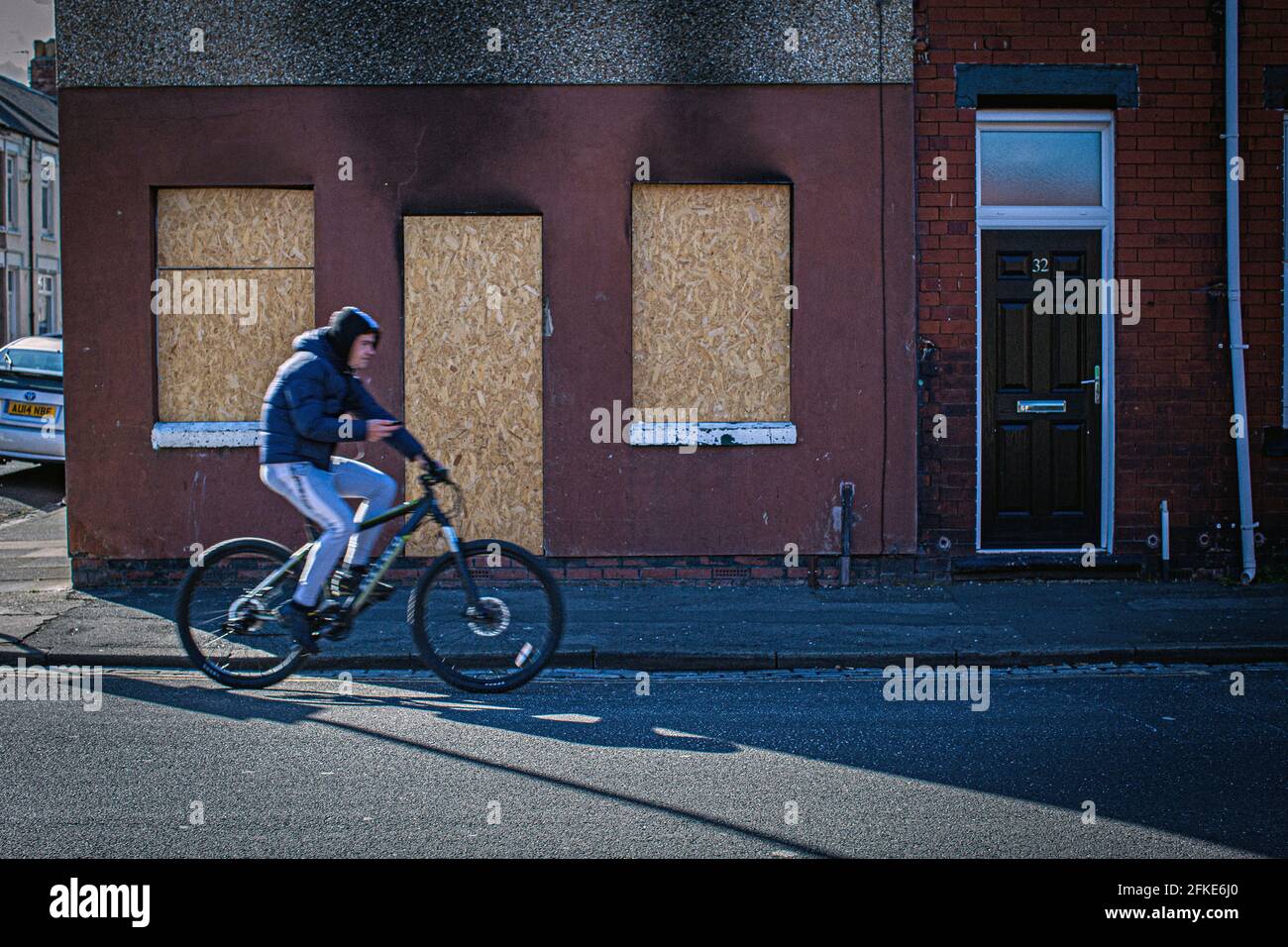 Man on bicycle passing boarded up windows and doors  at the most deprived streets , who are around the town centre in Hartlepool,County Durham, UK Stock Photo