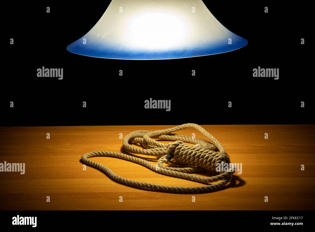 A noose lying on the table under a glowing chandelier, on a black background Stock Photo