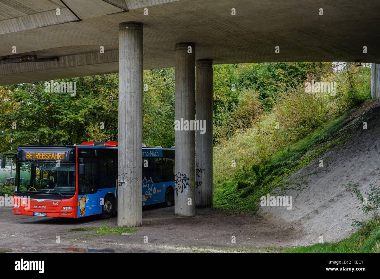 Parked passenger bus under a large concrete bridge. Stock Photo
