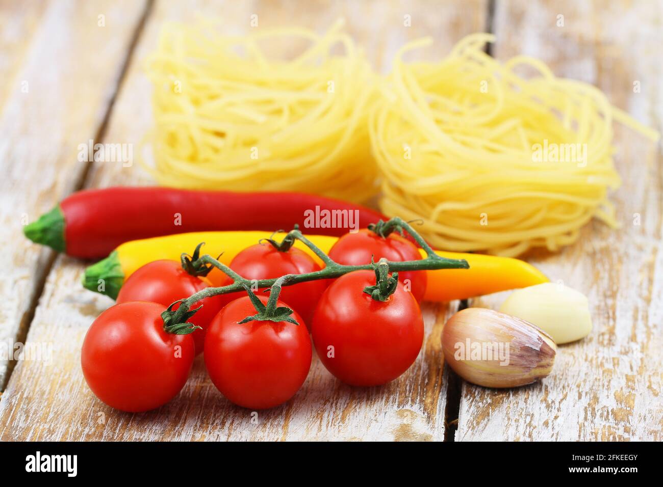 Selection of cooking ingredients: tagliatelle, cherry tomatoes, garlic cloves and chilies on wooden surface Stock Photo
