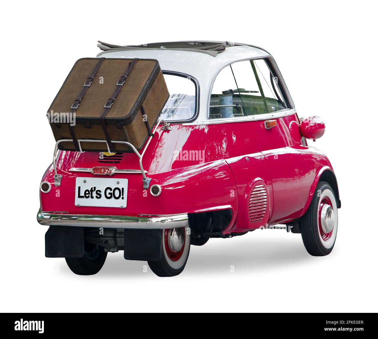 A small retro car with a suitcase attached to the back is ready for a trip, isolated on a white background. Stock Photo
