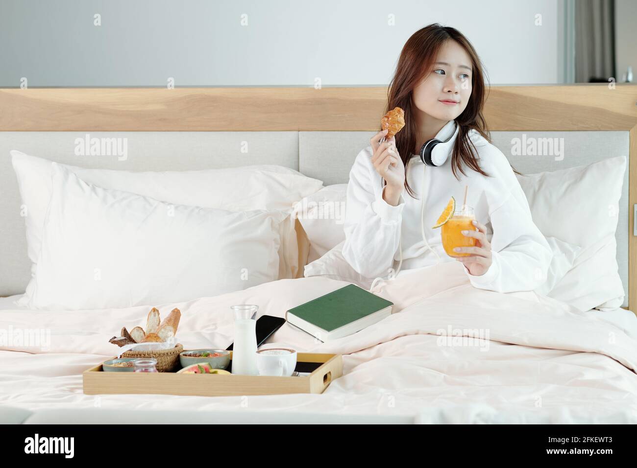 Pretty young woman eating croissant and drinking orange juice when