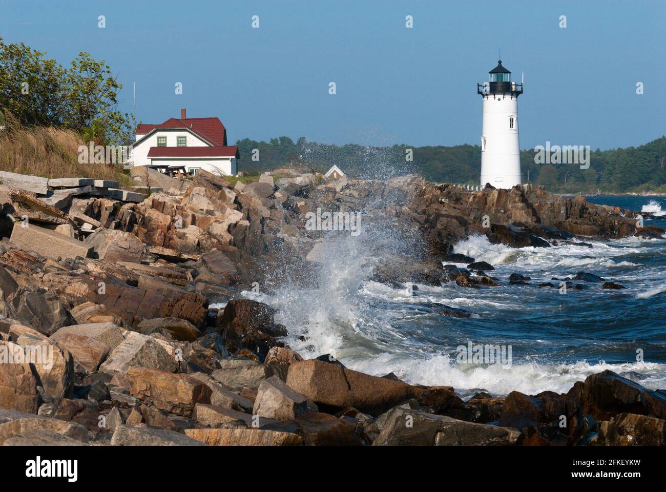 Large waves break over rocky shore by Portsmouth Harbor lighthouse, and nearby keepers quarters, which is now a US Coast Guard station in seacoast New Stock Photo