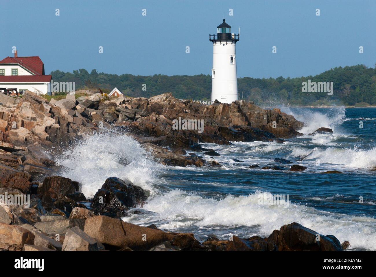 Large waves break over rocky shore by Portsmouth harbor lighthouse, also known as Fort Constitution light, and nearby keepers quarters, which is now a Stock Photo