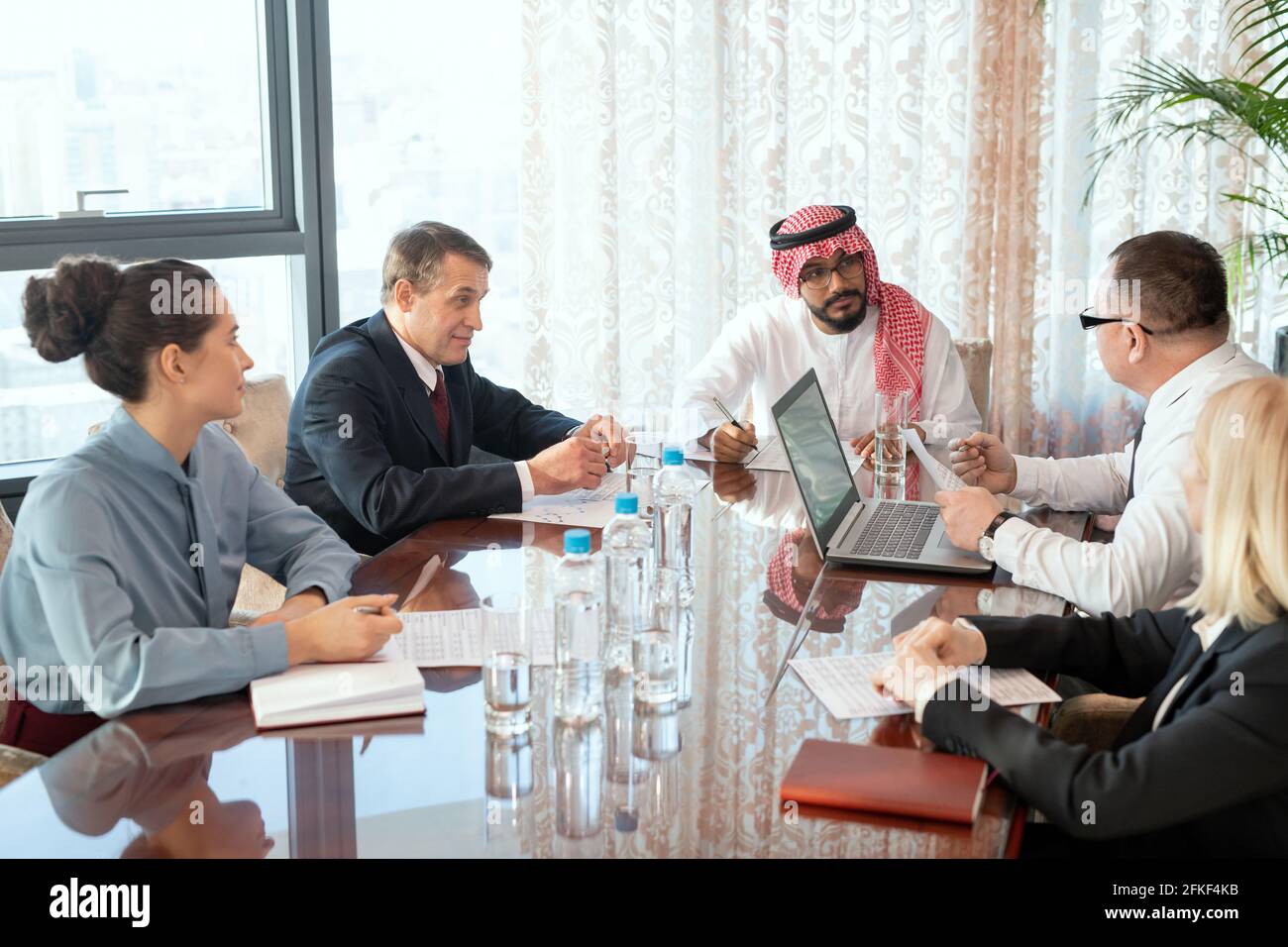 A group of delegates or businesspeople sitting around a table during meeting Stock Photo