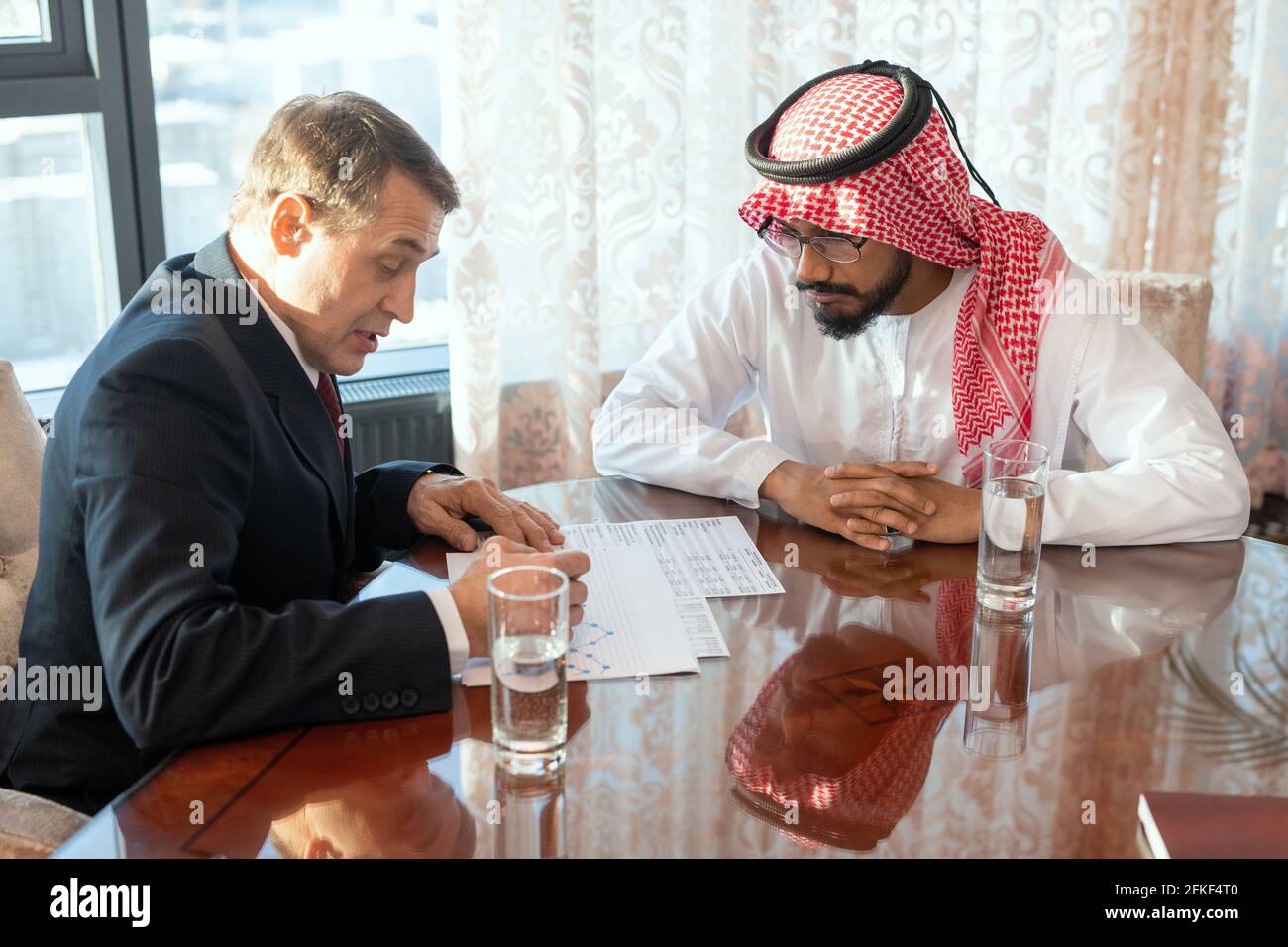 Two male delegates sitting at a table and discussing papers at working meeting Stock Photo