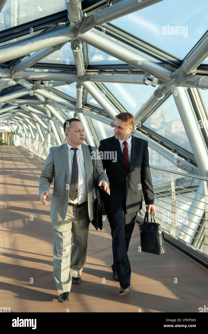 Men in suits walking down aisle inside modern building and talking Stock Photo