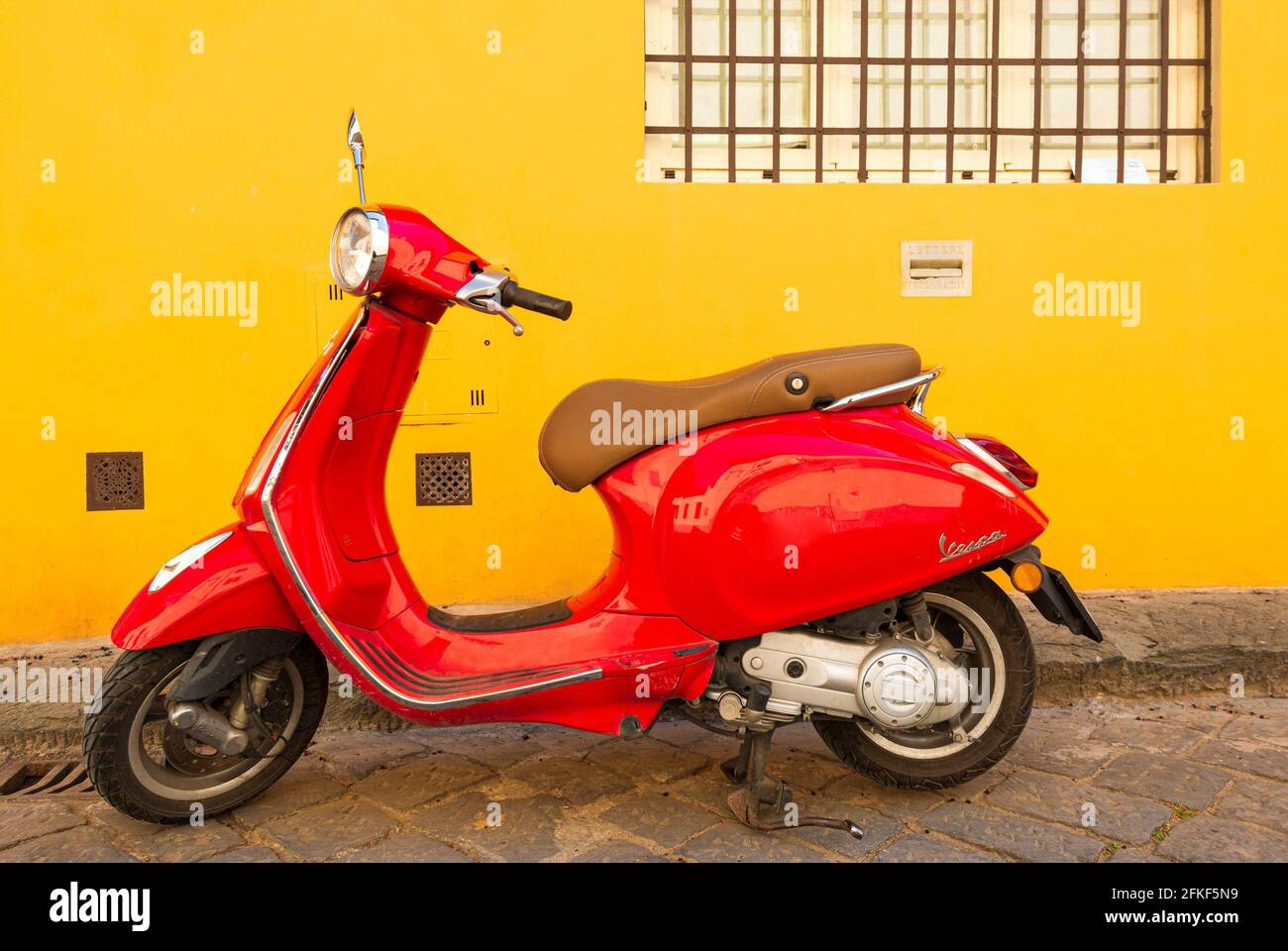 a red italian vespa is parked in a street of firenze in front of a yellow house in via san leonardo (italia) Stock Photo