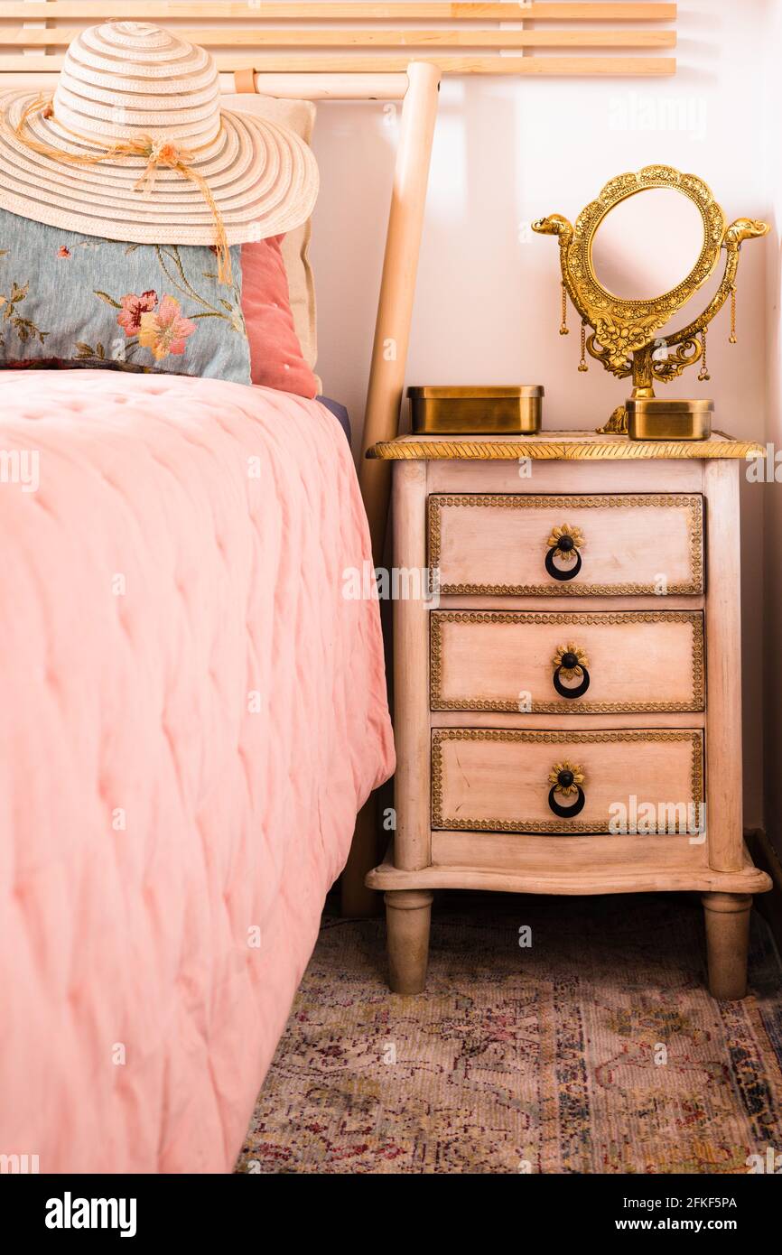 Stylish women sun hat lying on the bed next to the nightstand with a mirror. Elegance in a feminine style. Interior, Retro Stock Photo