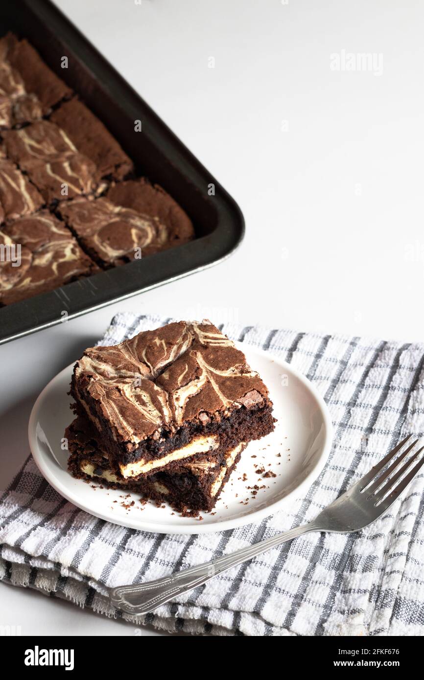 two cheesecake brownies on a white plate with a brownie tray in the background Stock Photo