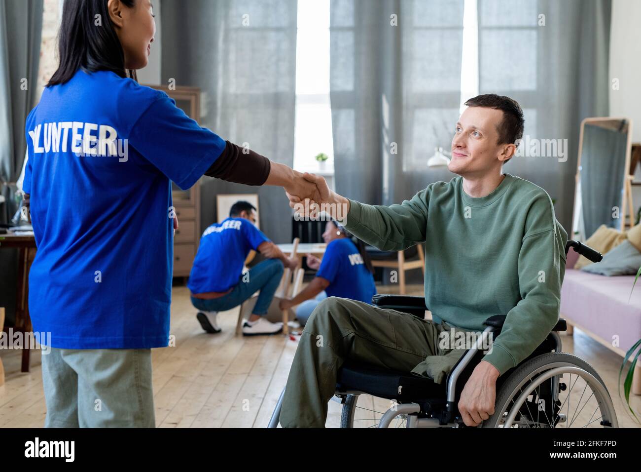 Young female volunteer shaking hand of man in a wheelchair Stock Photo