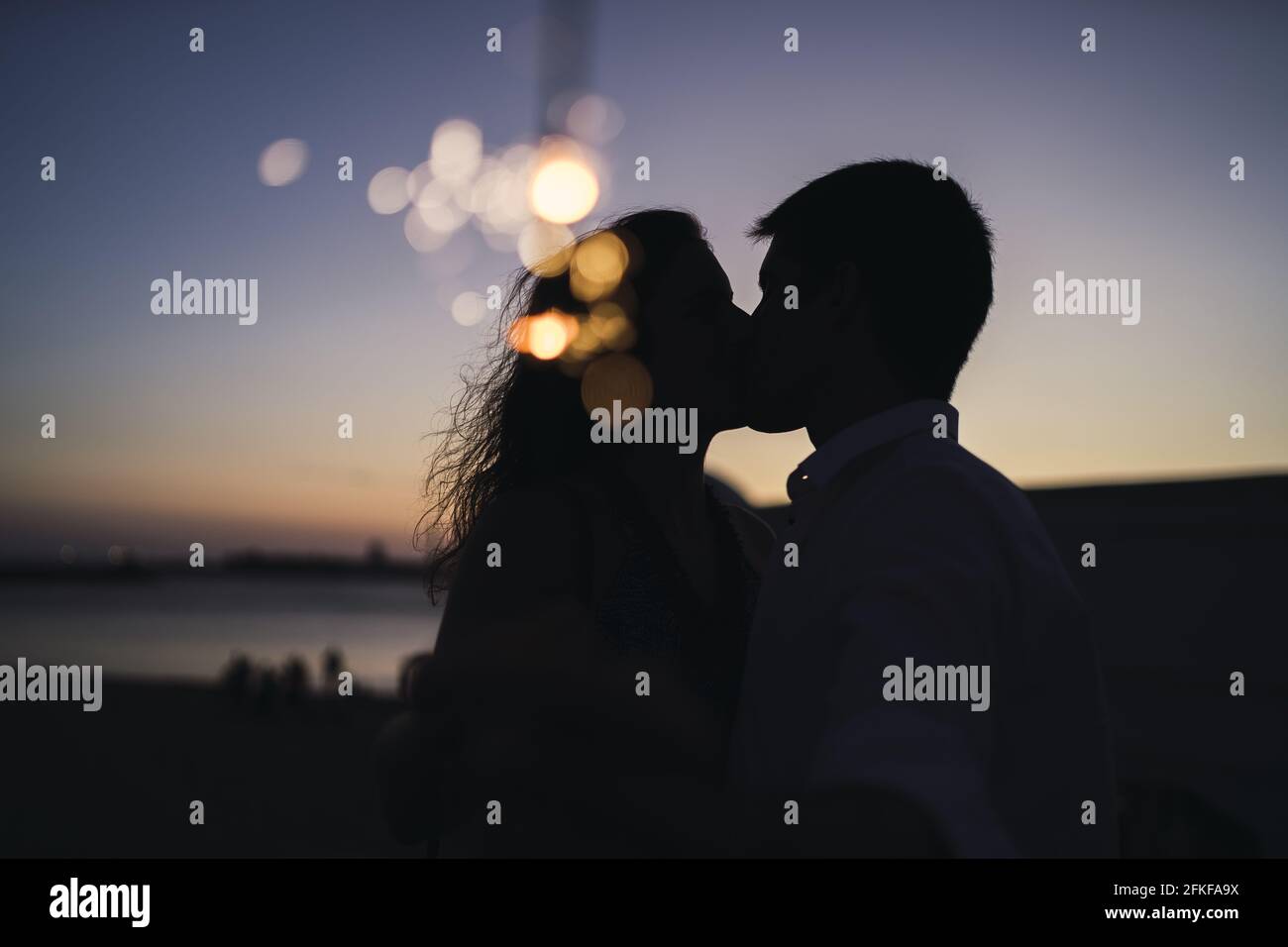 Silhouette of a young couple kissing at sunset; an image with bokeh ...