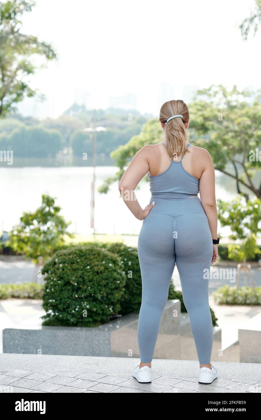 Fit plus size young woman looking at river, catching her breath and resting after jogging, veiw from the back Stock Photo