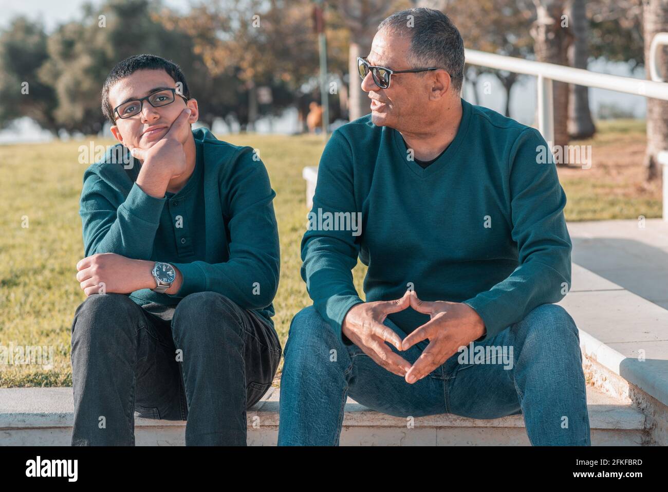 Teenager son and senior father sitting on stairs outdoors at home and talking. Stock Photo