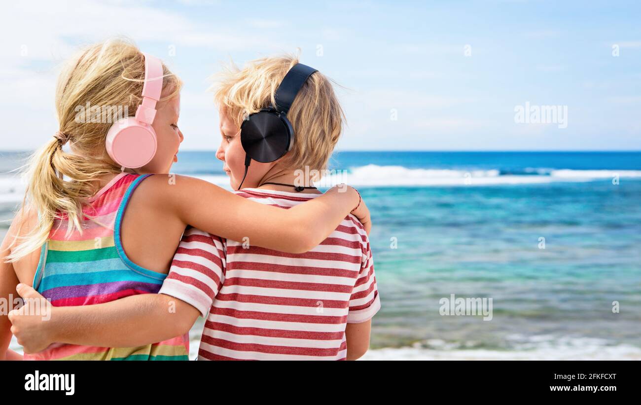 Young positive kids in headphones listening music with fun at tropical beach party. Travel family lifestyle, recreational activities at summer cruise Stock Photo