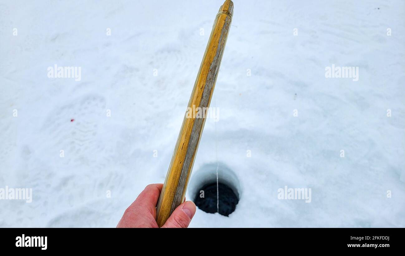 Mans hand holds a old school ice fishing rod with line going