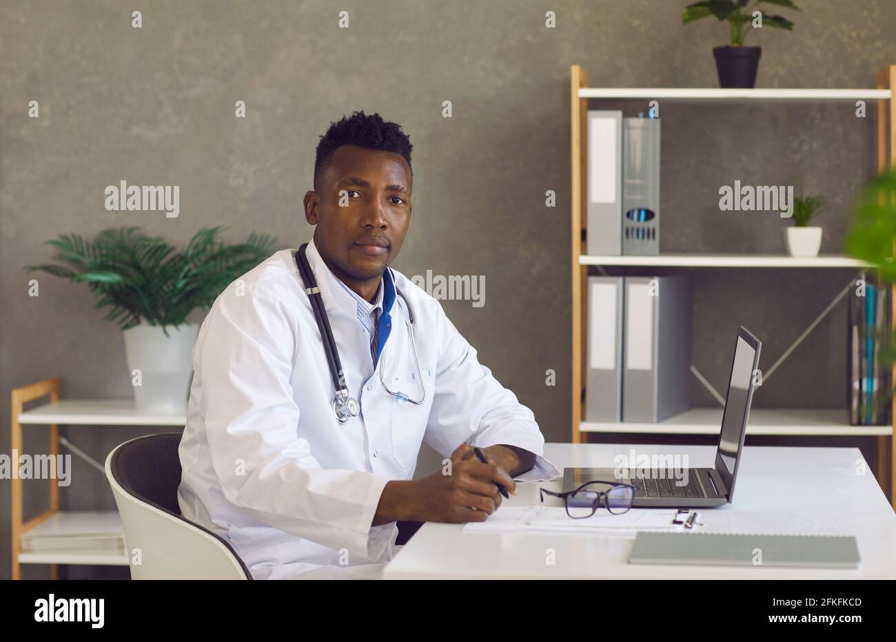 Serious young African American doctor sitting at desk with laptop and looking at camera Stock Photo