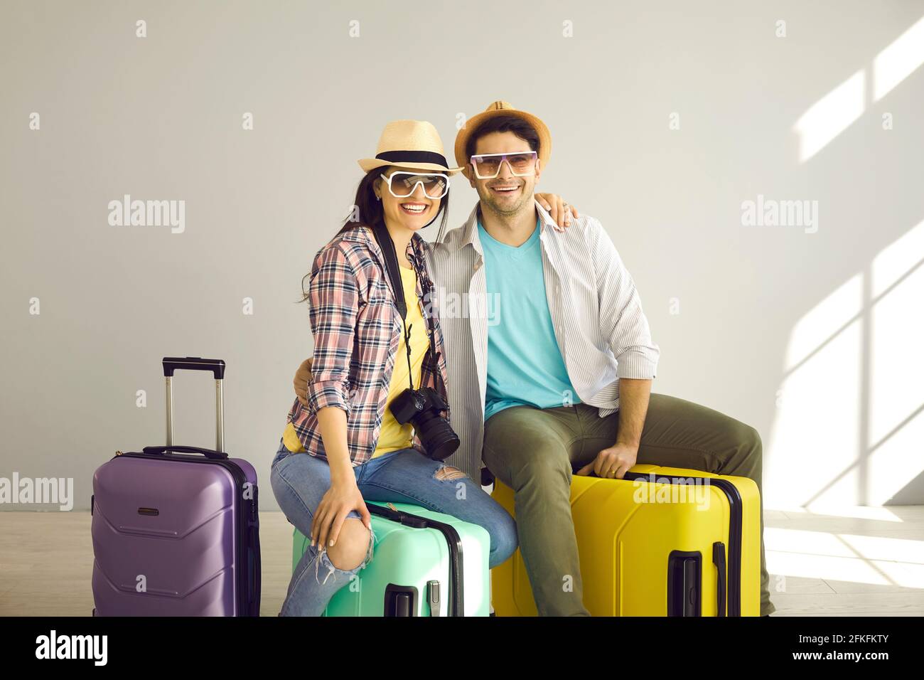 Studio portrait of happy young couple sitting on suitcases packed for holiday trip Stock Photo