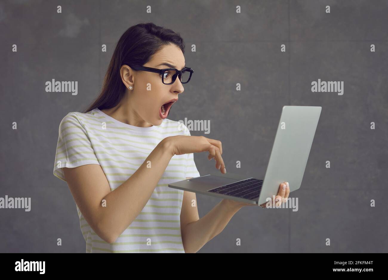 Shocked emotional woman in eyeglasses looking at laptop screen studio shot Stock Photo