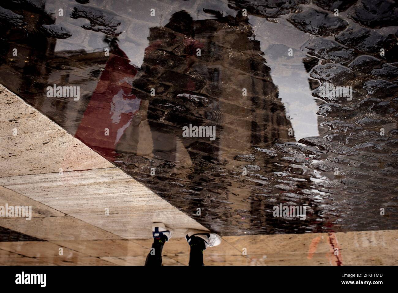 A demonstrator holding a red communist flag is seen reflected in a puddle of water during May Day 2021 in Barcelona. Stock Photo