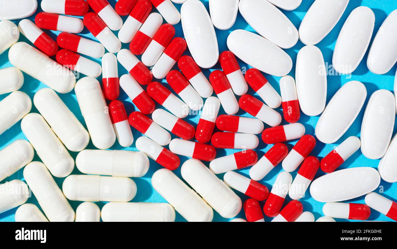 Red and white capsules and white pills on blue background Stock Photo