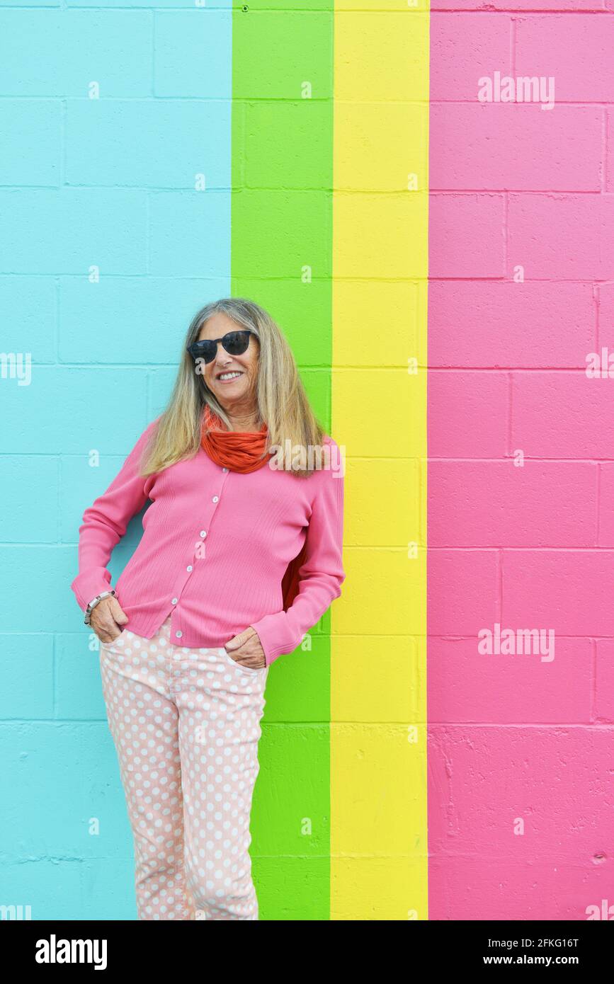 Attractive senior woman posing against brightly colored striped wall outdoors Stock Photo