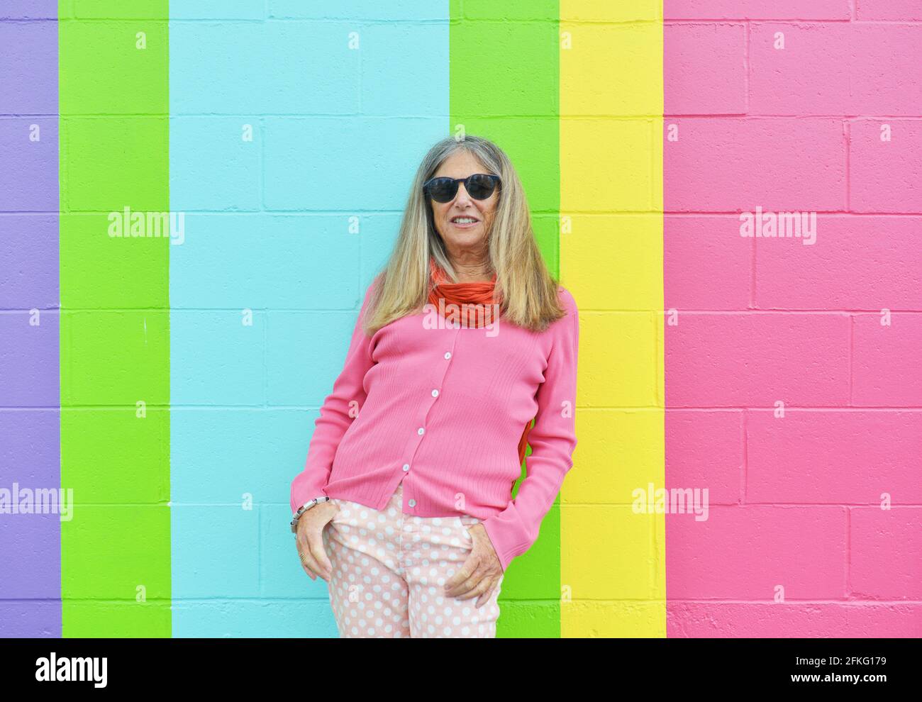 Attractive senior woman posing against brightly colored striped wall outdoors Stock Photo