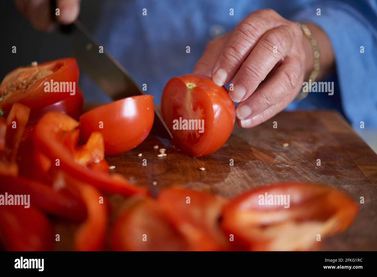 Senior older woman chopping vegetables in modern kitchen. Closeup of tomatoes. Stock Photo