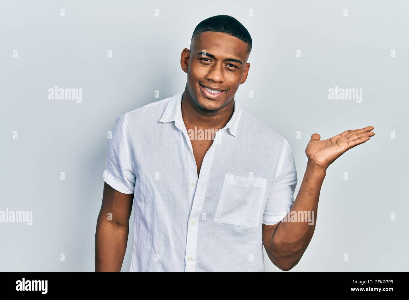 Young black man wearing casual white shirt smiling cheerful presenting ...