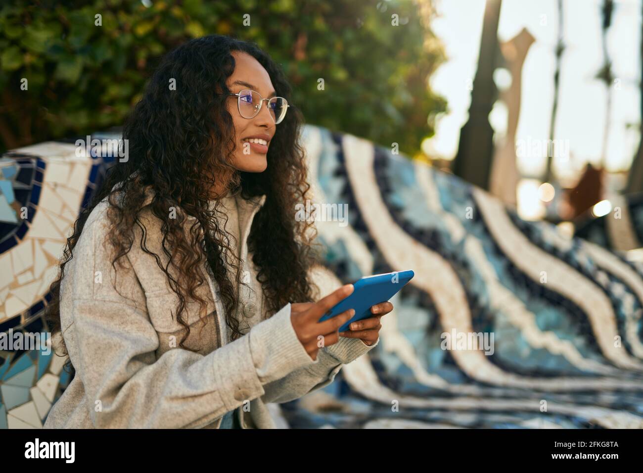Young latin woman smiling happy using touchpad sitting on the bench at ...