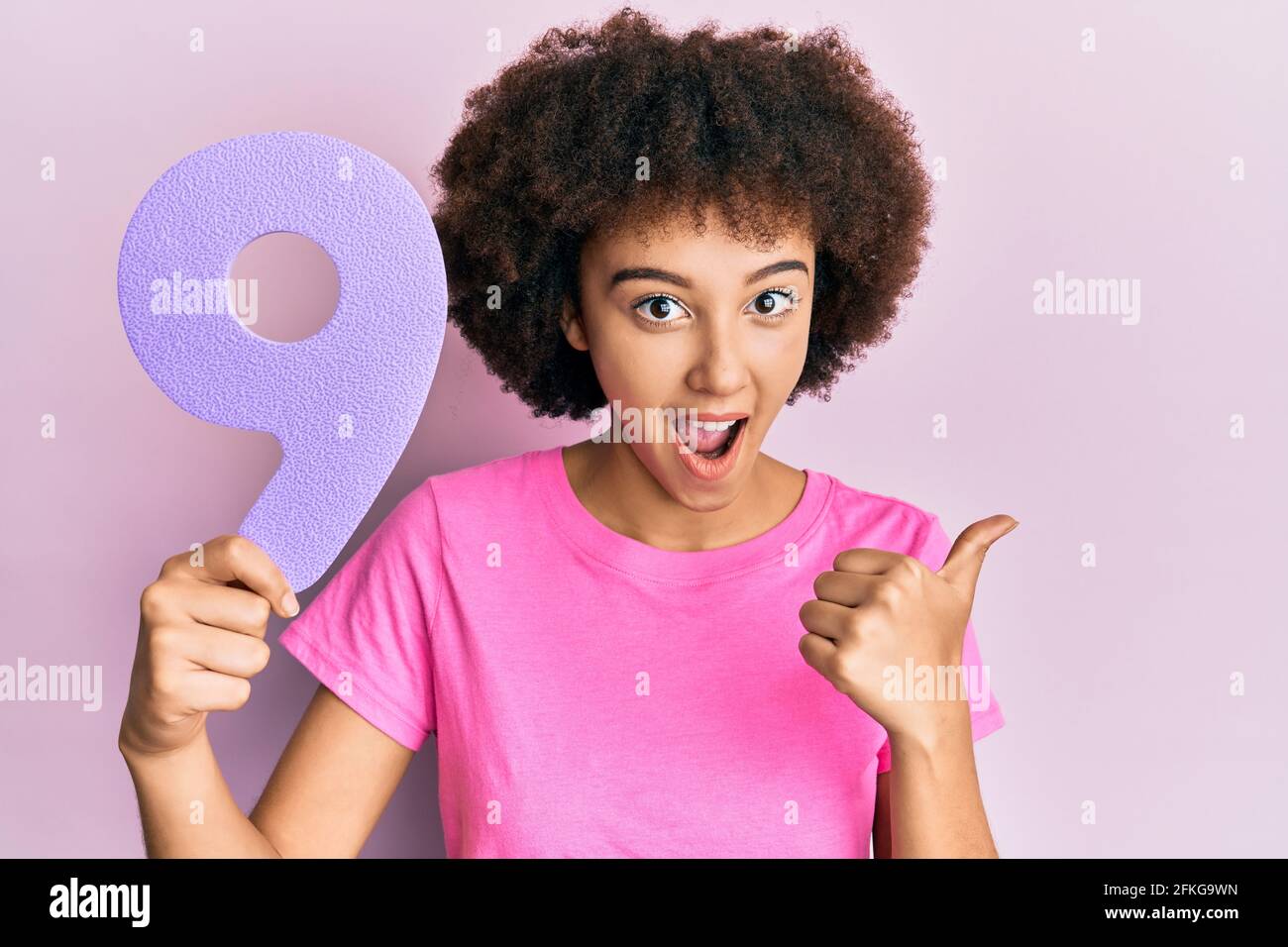 Young hispanic girl holding number nine pointing thumb up to the side ...