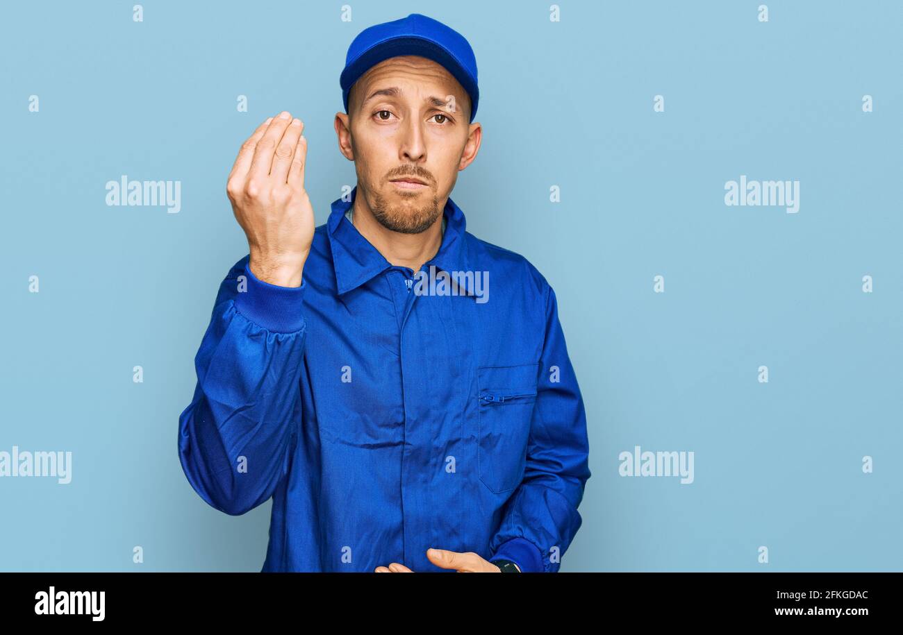 Bald man with beard wearing builder jumpsuit uniform doing italian gesture with hand and fingers confident expression Stock Photo