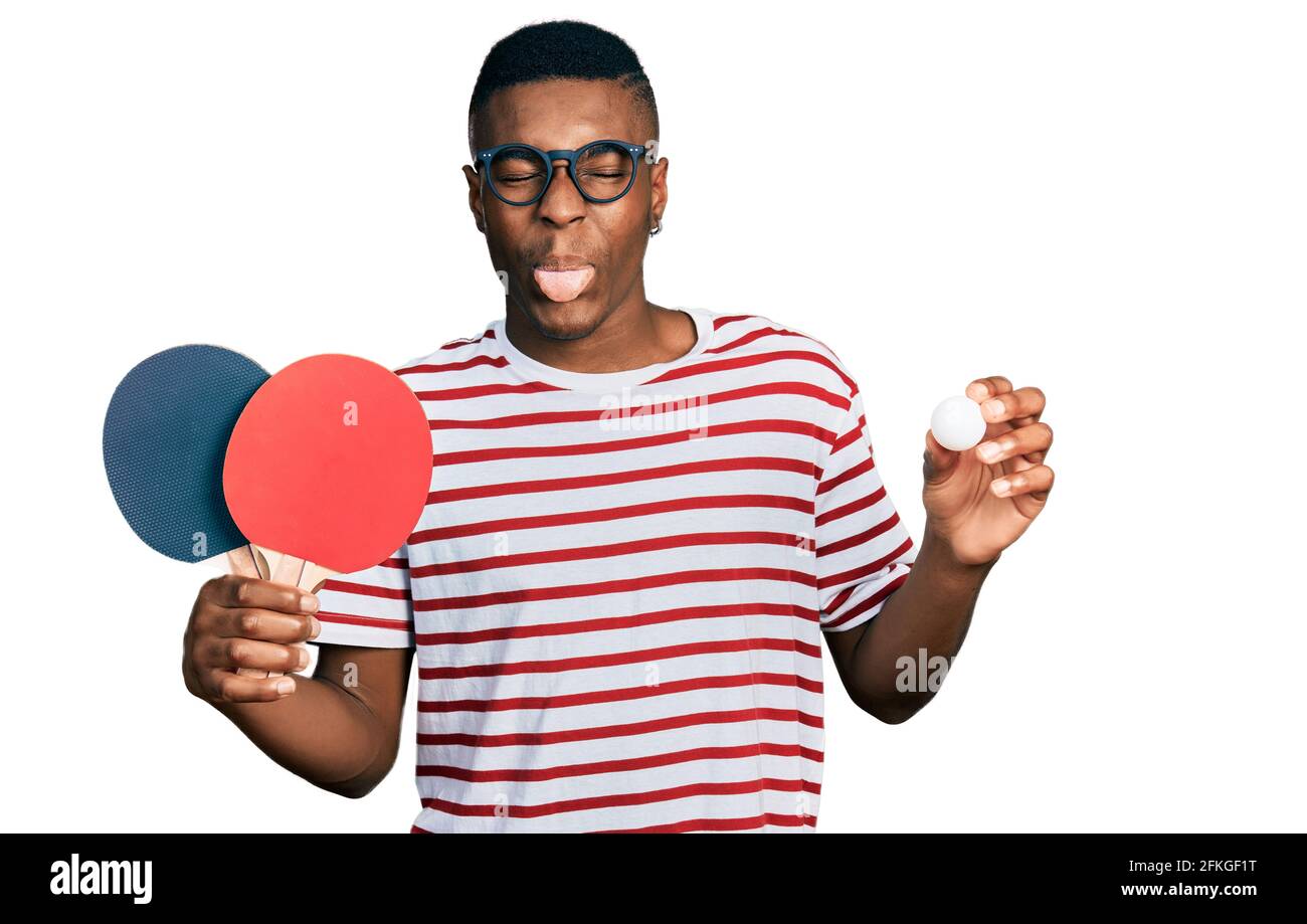 Young african american man holding red ping rackets and ball sticking tongue out happy with funny expression Stock Photo Alamy