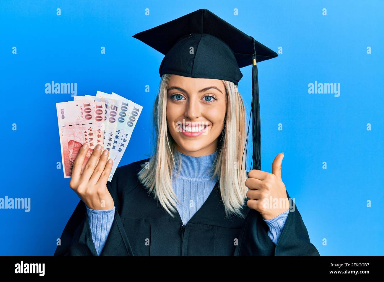 Beautiful blonde woman wearing graduation cap and ceremony robe holding ...