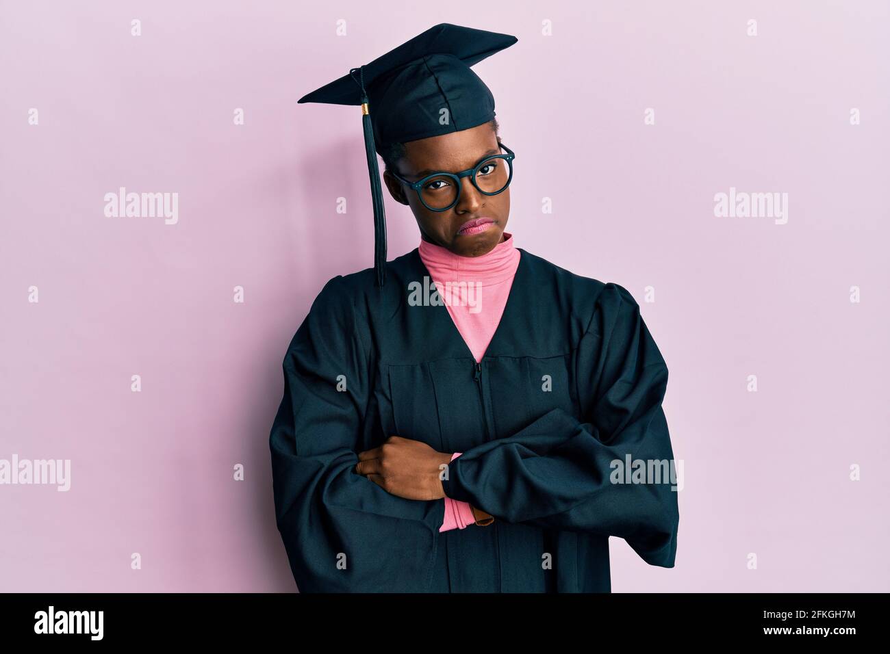 Young african american girl wearing graduation cap and ceremony robe skeptic and nervous, disapproving expression on face with crossed arms. negative Stock Photo