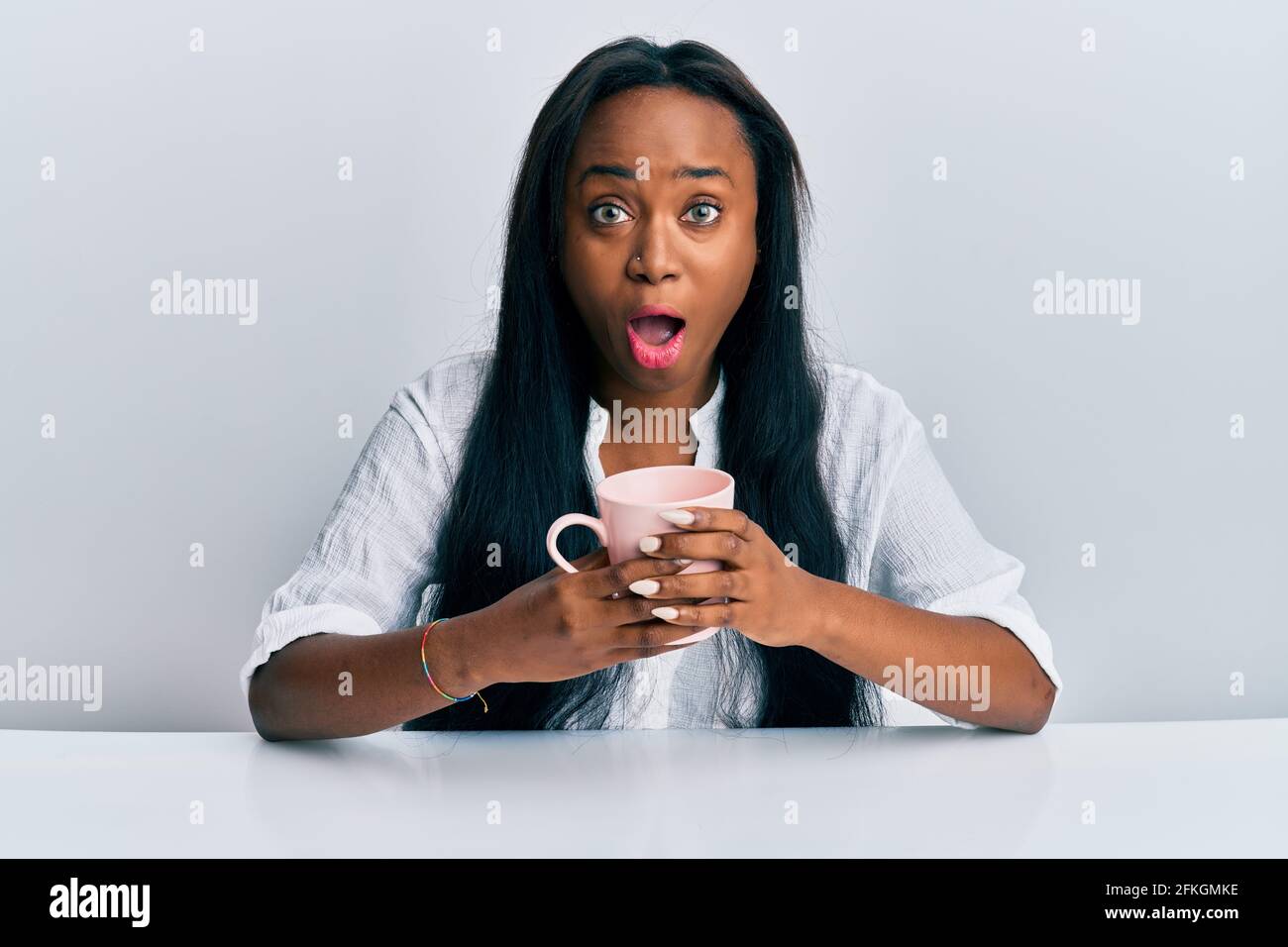 Young african woman drinking a cup coffee afraid and shocked with