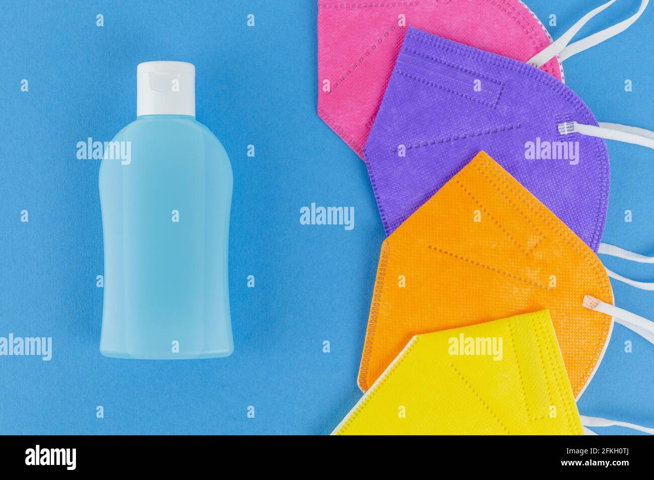 Hand alcohol sanitizer and different colors FFP2 or N95 face masks respirators. on blue background. Top view flat layer. Protection from covid virus d Stock Photo