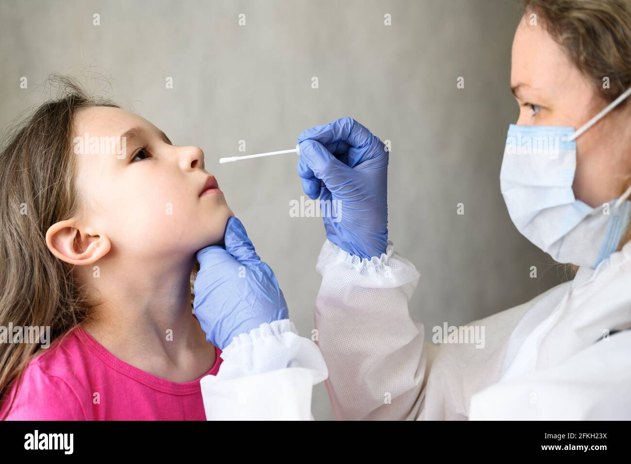 COVID-19 PCR test and kid, nurse holds swab for nasal sample from adorable child. Woman doctor in PPE suit examines cute little girl during coronaviru Stock Photo