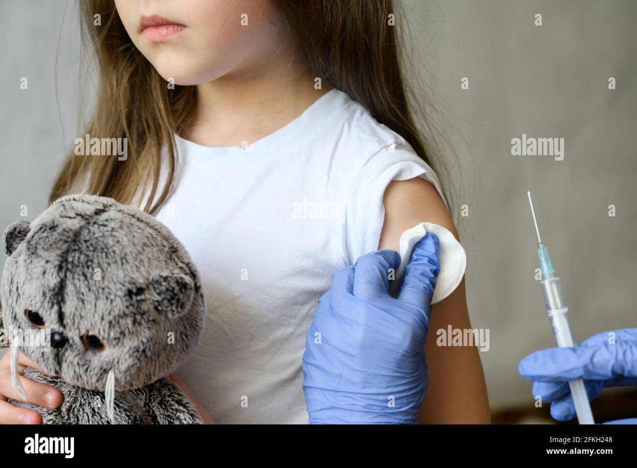 Kid and COVID-19 vaccination, cute little girl during coronavirus vaccine injection. Doctor holds syringe to make jab to adorable child. Concept of im Stock Photo
