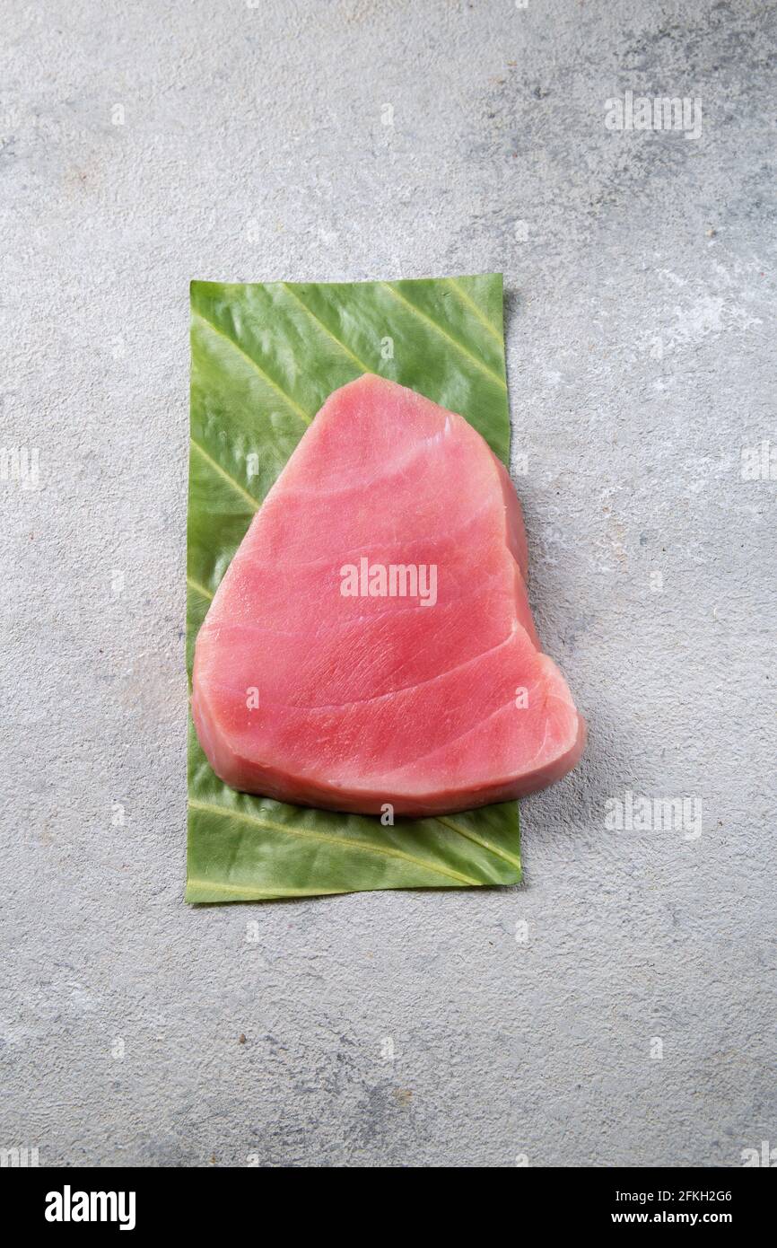 Raw tuna steak on green leaf, grey background Stock Photo