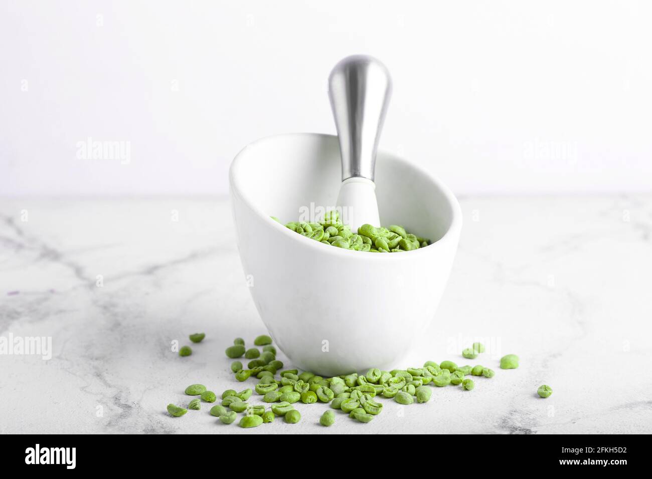 Mortar and pestle with green coffee beans on light background Stock
