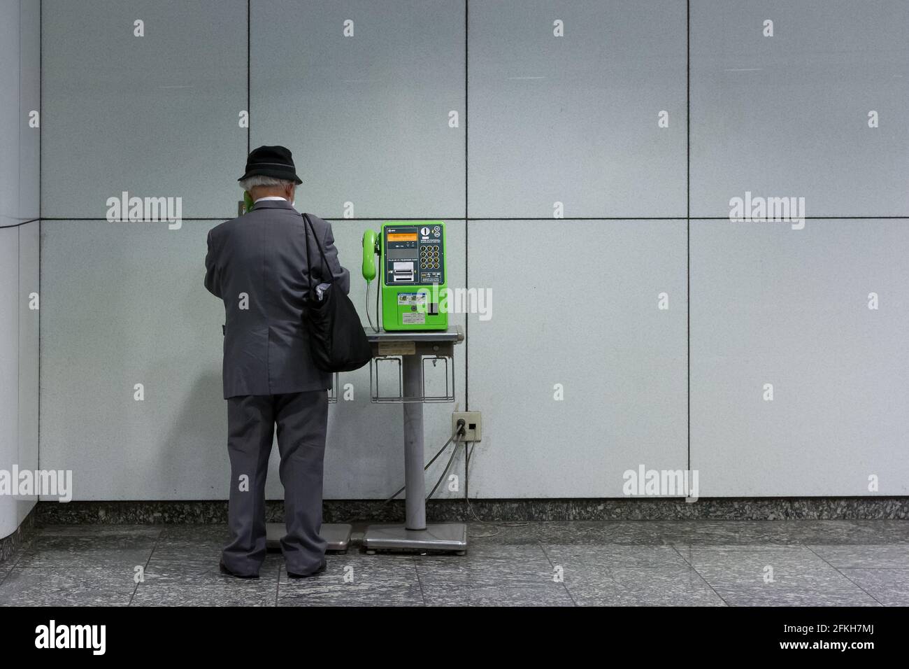 An older Japanese man uses a payphone in Shinjuku Station, Shinjuku, Tokyo, Japan. Stock Photo