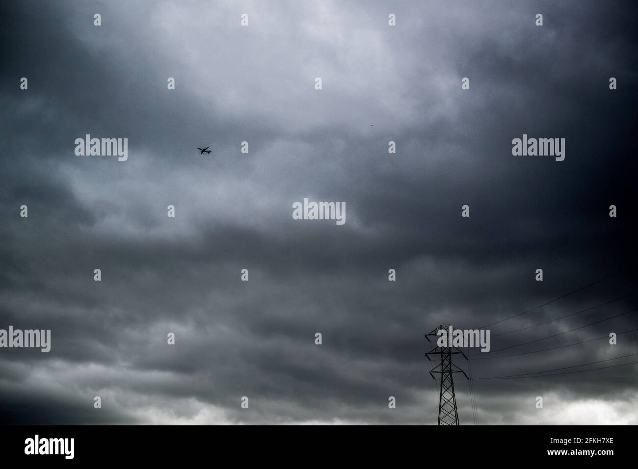 Airplane and electricity pylon against dark grey cloudy sky Stock Photo ...