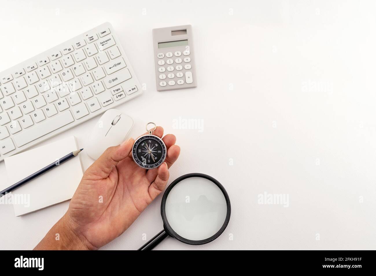 Businessman looking at a compass which he is holding in his hand, Businessman with a compass holding in hand on Business objects White table backgroun Stock Photo
