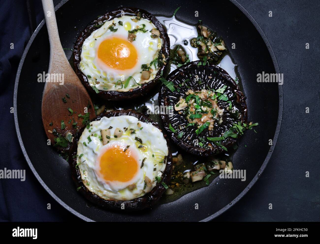 A pan with fried eggs and portobello mushrooms on dark background